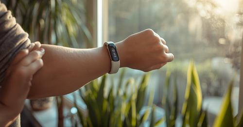 Person checking fitness wristband health data by window in natural morning light
