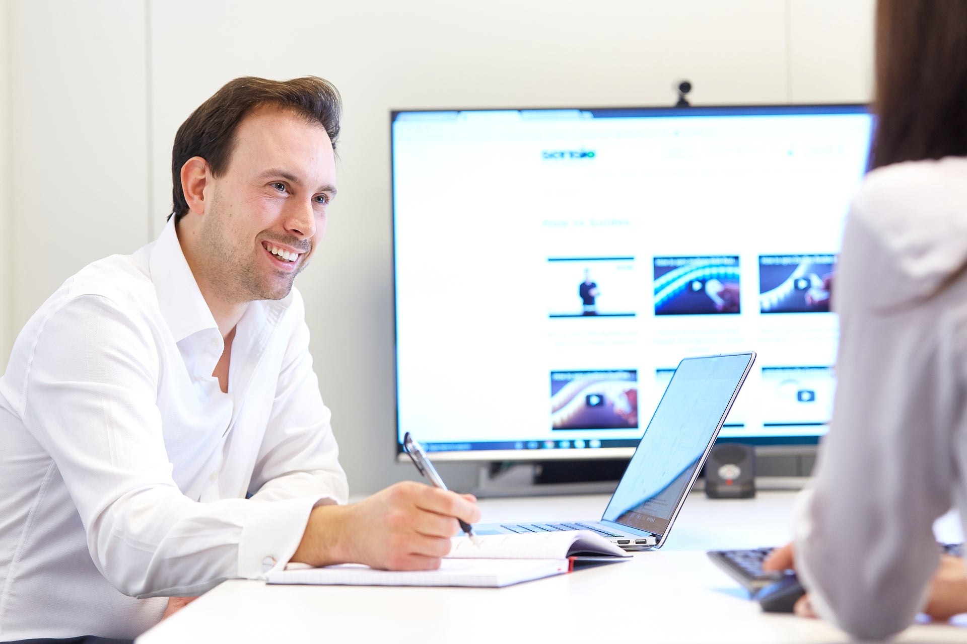 Two people working together at a desk with a laptop and computer monitors.
